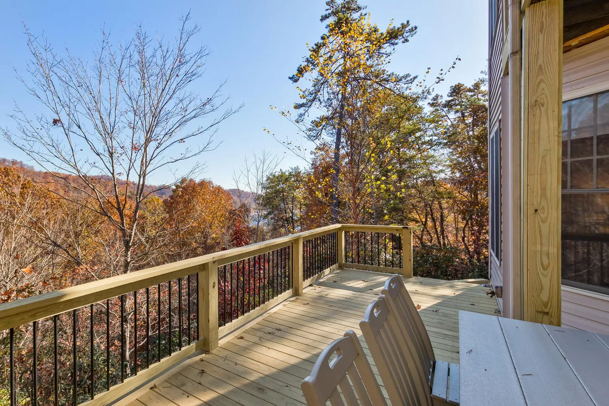 A spacious wooden deck surrounded by vibrant autumn trees, with a distant lake view. The deck is designed for relaxing, reading, or socializing, and provides a peaceful setting that blends nature with comfort.