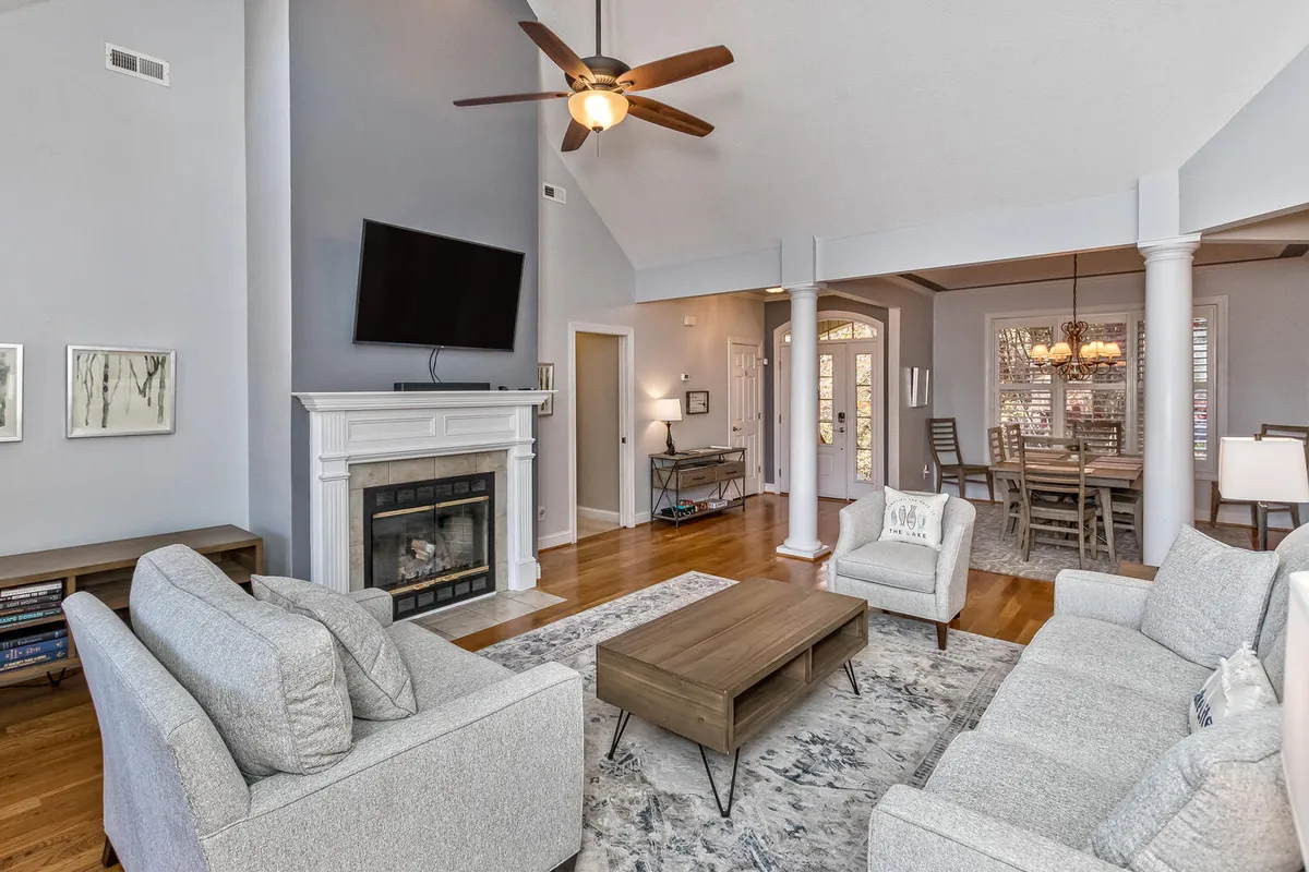 A stylish interior featuring a fireplace, coordinated sofa set, dining area, ceiling fan, and eye-catching wall art. The space is arranged for both relaxation and entertaining, with areas for gathering, dining, and enjoying time together.