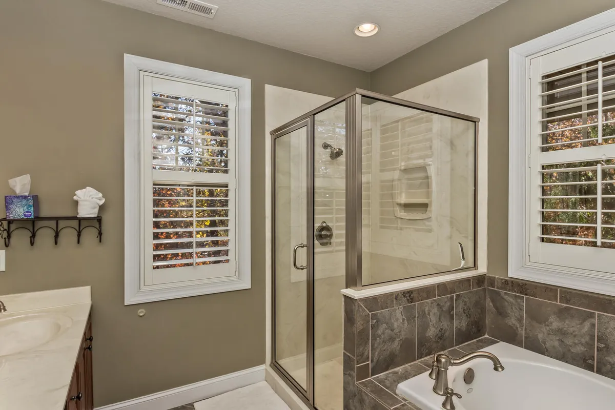 A luxurious bathroom featuring a standalone bathtub, glass-enclosed shower, and window with shutters. The serene setting invites guests to indulge in relaxing baths or revitalizing showers, echoing a spa-like experience in a private retreat.