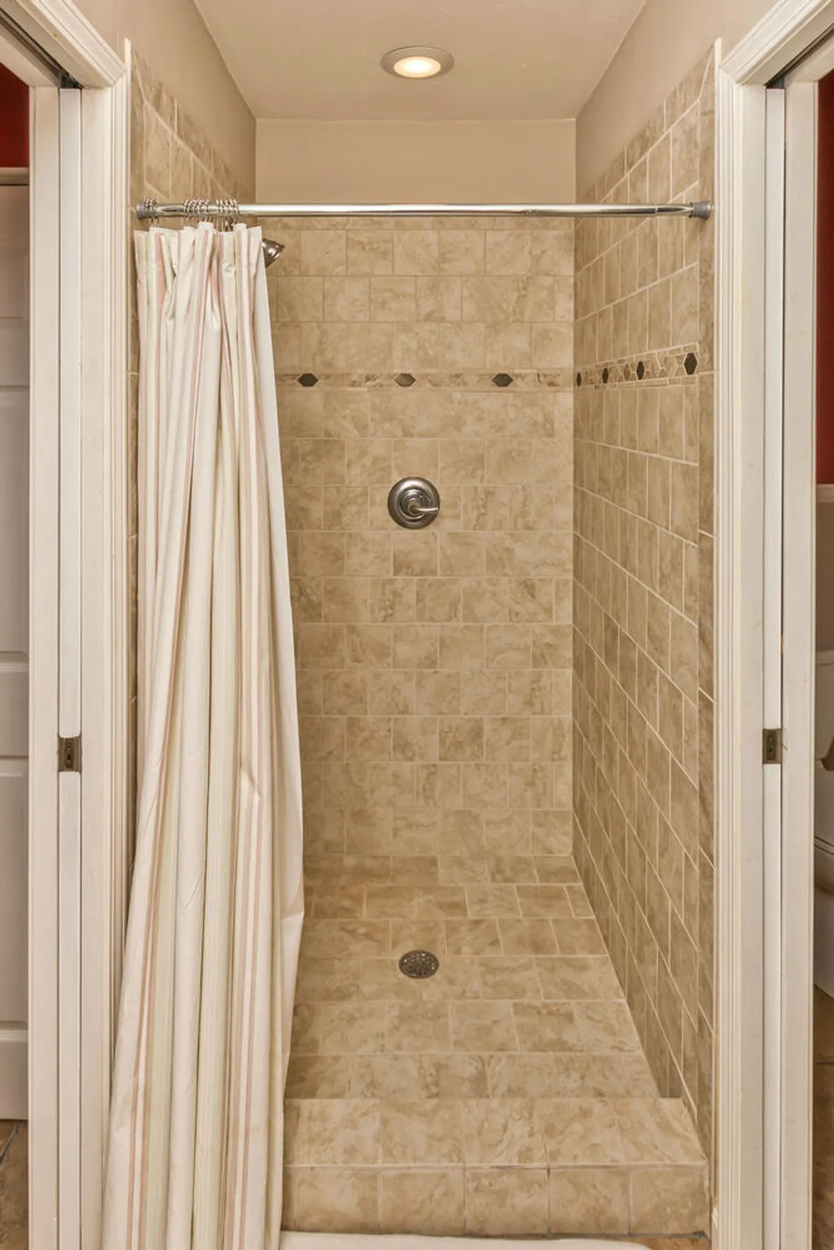 A modern tiled shower area with a simple shower curtain and clean, inviting tile work. The space is serene and designed for refreshing self-care routines.