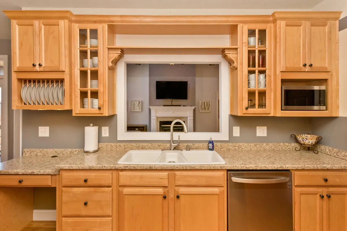 A perspective from the kitchen showing granite countertops, wooden cabinets, a sink, and clear open sightlines to the adjacent living or dining area, emphasizing the kitchen's connection to communal spaces.