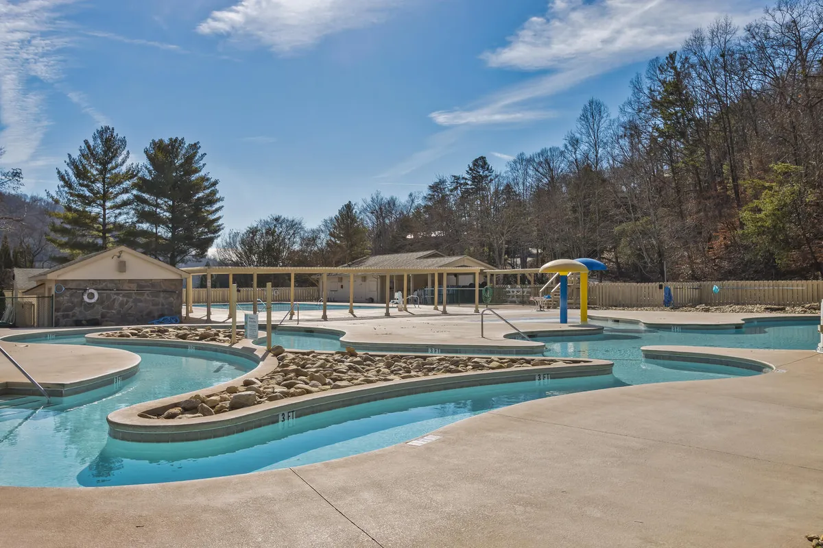 A curved swimming pool bordered by natural rock formations and featuring exciting water slides. The pool area is spacious, with room for sunbathing and social gatherings, and is surrounded by lush landscaping that gives it a resort-like atmosphere.