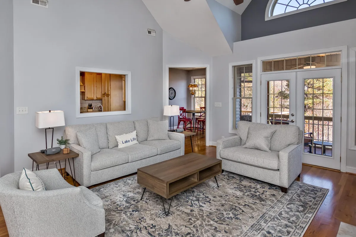 An inviting open-plan space featuring comfortable sofas, a coffee table, a large window with views of the outdoors, and a visible adjoining dining area. The overall ambiance is warm and inclusive, with natural light streaming into both the living and dining areas.