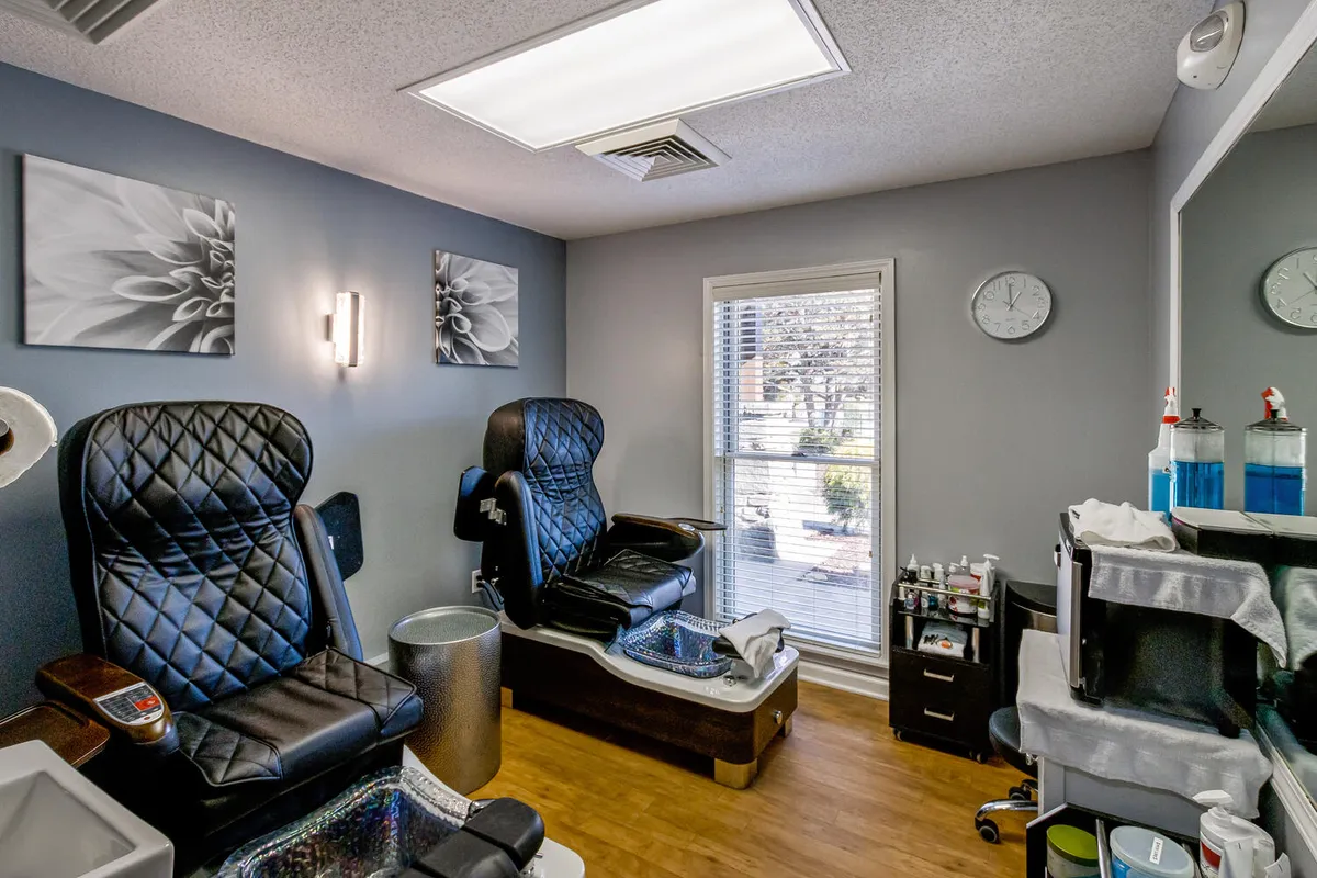 Inside the spa, luxurious pedicure chairs bask in natural light from a large window, with tasteful artwork adorning the walls. The atmosphere is calm, inviting, and perfect for self-care and relaxation.
