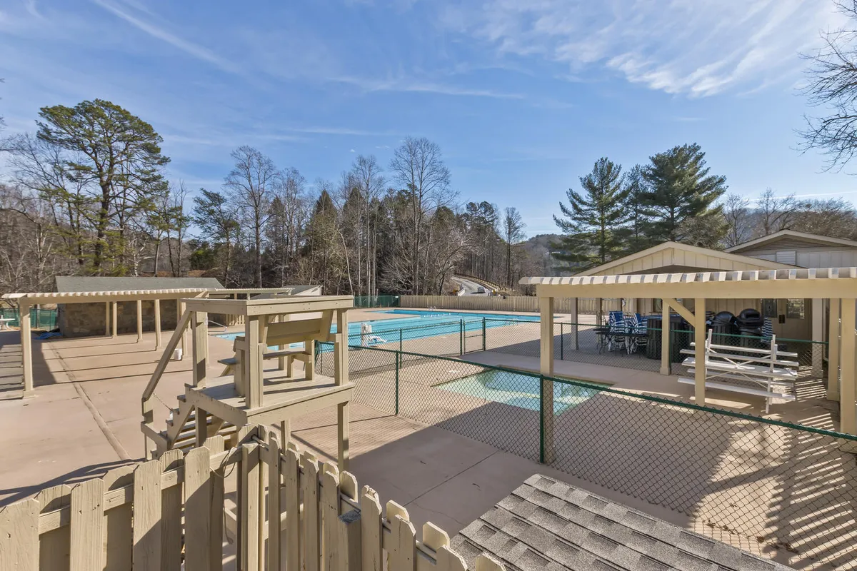This image captures a large swimming pool surrounded by lounge chairs, fencing, and lush trees. The pool area appears inviting and spacious, perfect for families to relax, swim, and socialize during sunny afternoons.